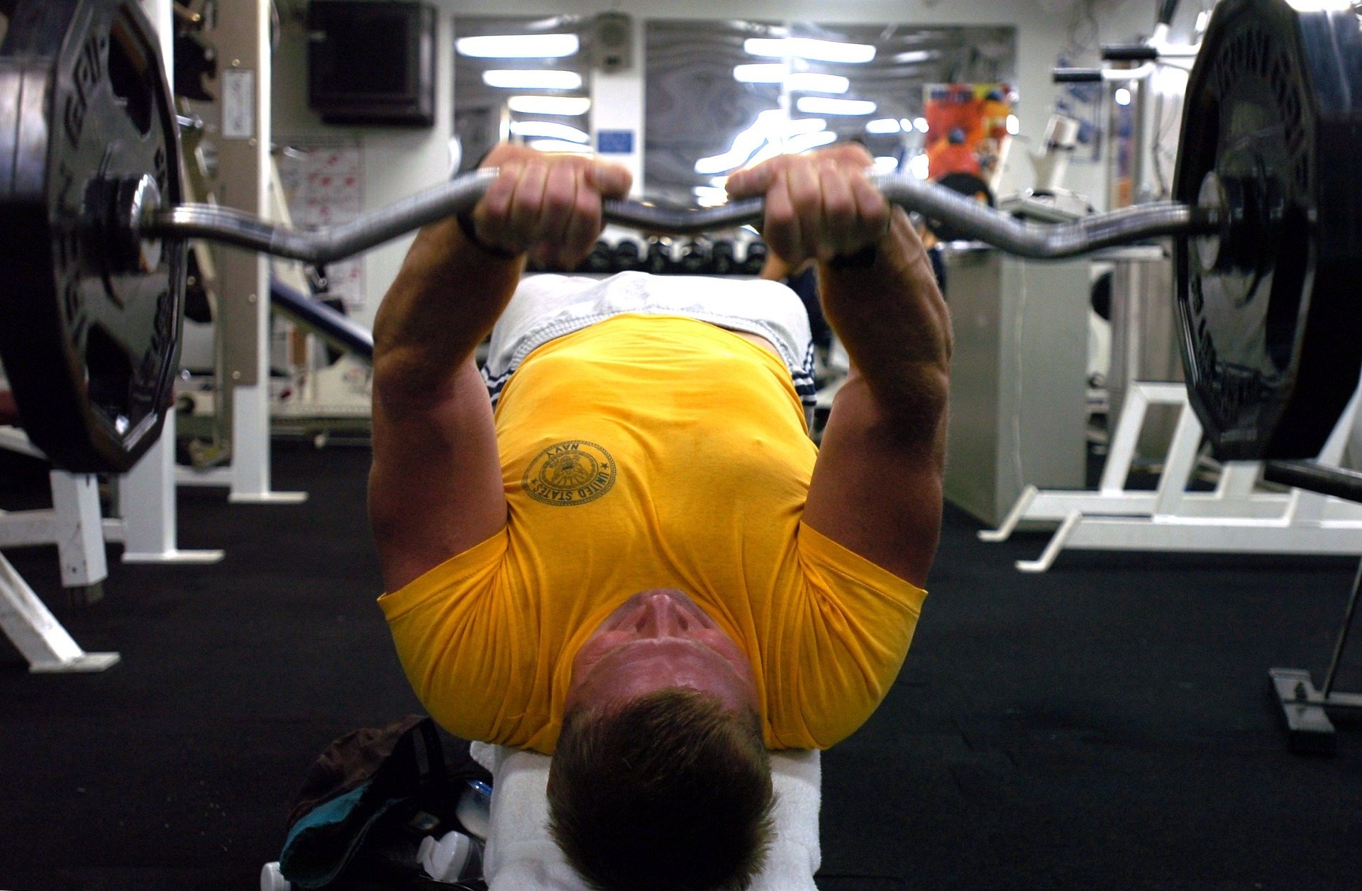 man in geel t-shirt in sportschool die triceps aan het trainen is met een ez barbell
