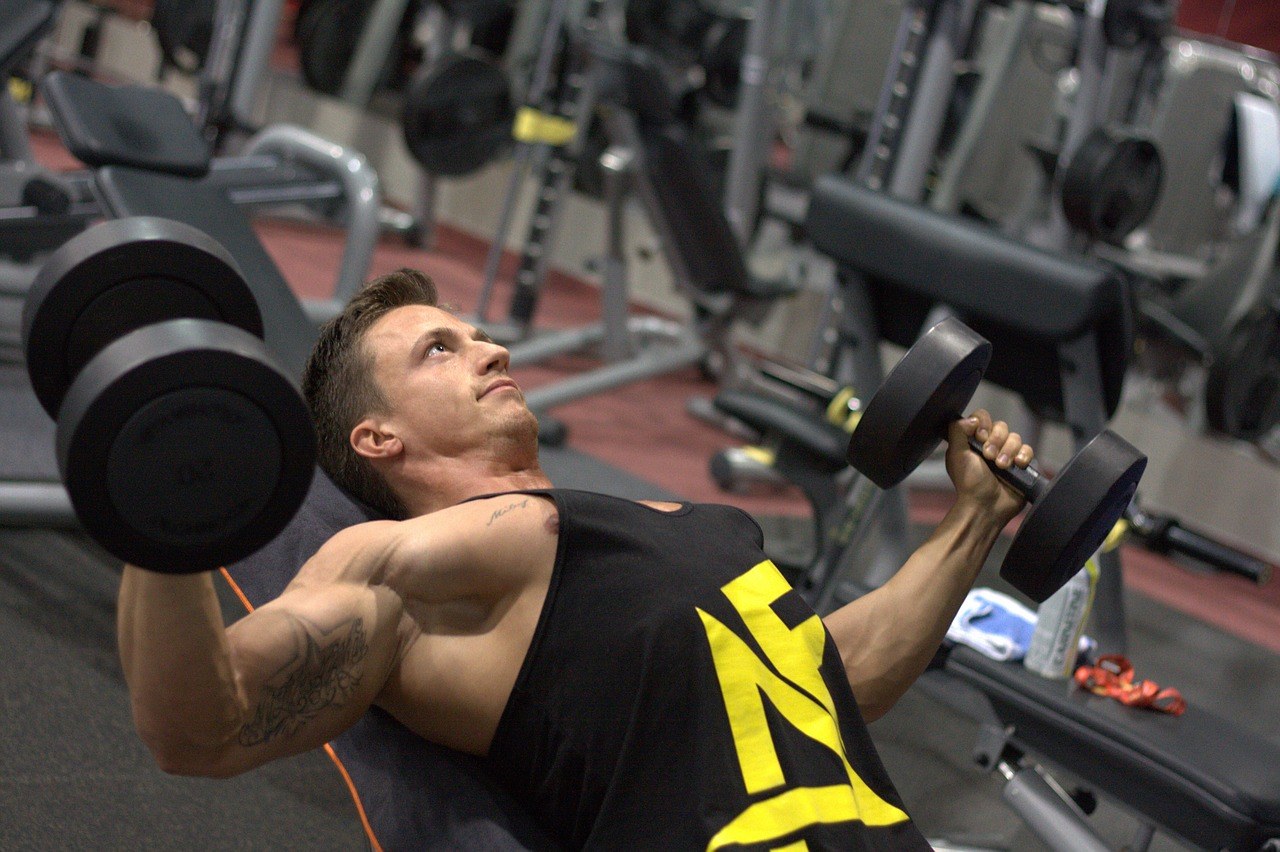 bovenkant borst trainen in de sportschool door een man in een zwarte tanktop met dumbbells