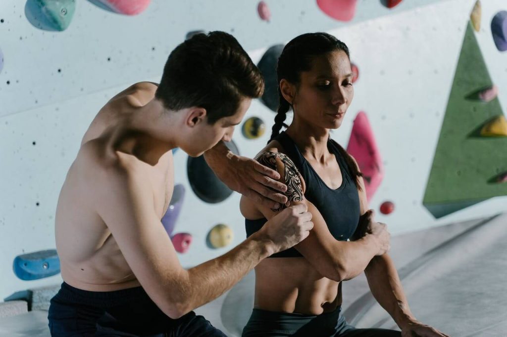Man en vrouw in klimhal die sporten met spierpijn en elkaar helpen