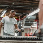 Fitness tips van een man in grijs shirt in de sportschool die biceps traint met dumbbells