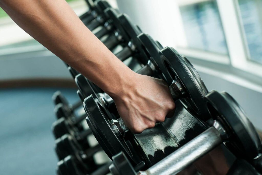 Persoon neem dumbbells uit een rek in de sportschool
