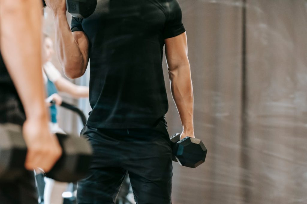 Man in de sportschool gebruikt dumbbells en heeft bepaald hoeveel sets per spiergroep per week hij moet trainen voor sterkere biceps