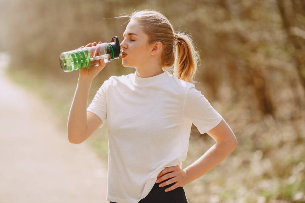Jonge vrouw in wit t-shirt drinkt water uit een sport bidon