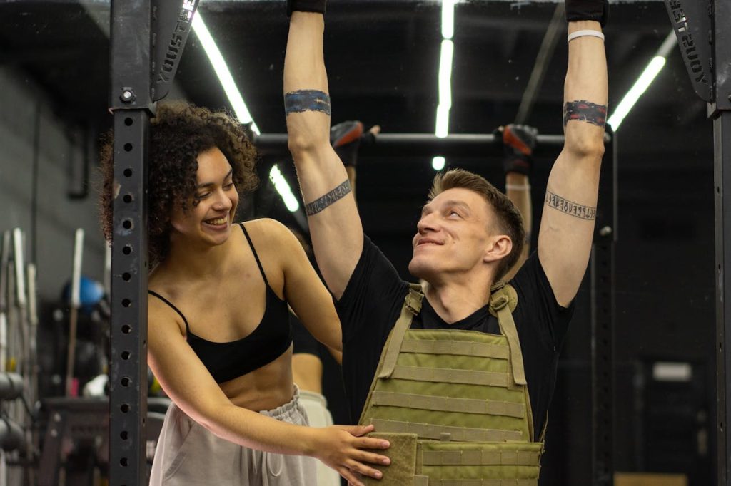 Man doet pull-ups met gewichtsvest en krijgt hulp van personal trainer