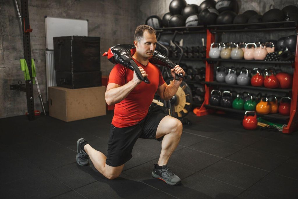 Man in rood shirt doet lunges met een bulgarian bag