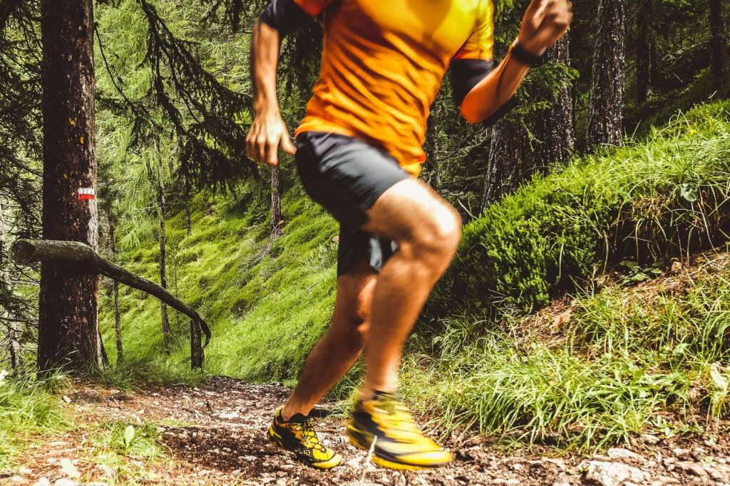 Man in het bos aan het hardlopen in oranje shirt en korte broek