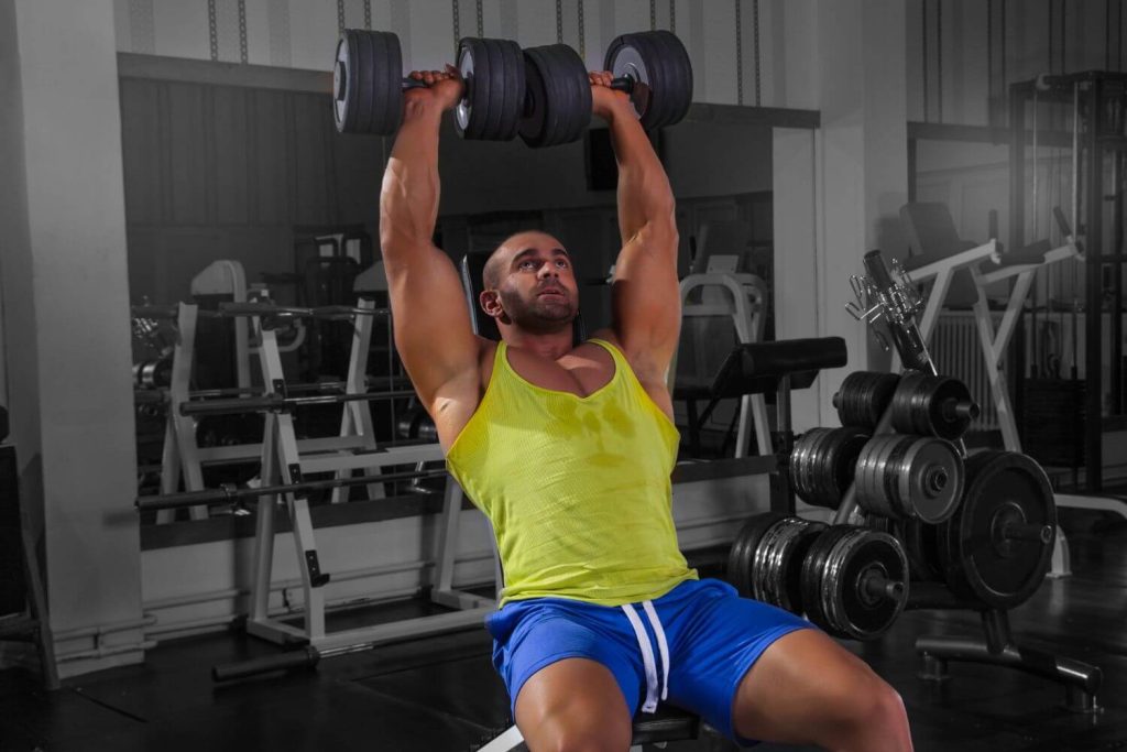 Man in gele tanktop doet een Arnold press