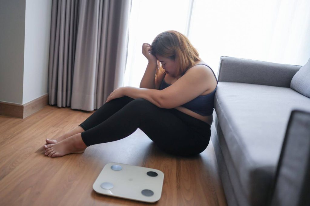 vrouw merkt het jojo-effect en is weer aangekomen en zit daarom ontevreden op de grond naast de weegschaal