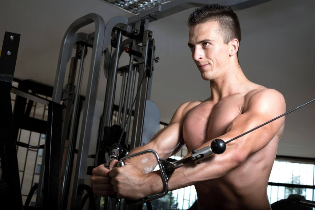 Fitte man doet een standing cable fly in een sportschool met een kabelstation