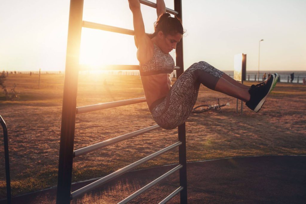 Hanging knee raises door een vrouw aan een rek in de buitenlucht