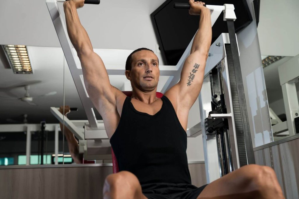 Man in zwarte tanktop op een machine shoulder press