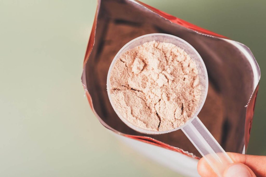 persoon neemt een scoop clear whey aardbei uit een stazak